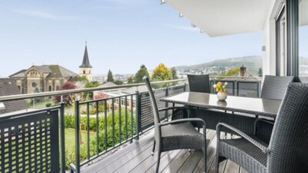 A balcony with a table and chairs, a view of a church, and a clear sky.