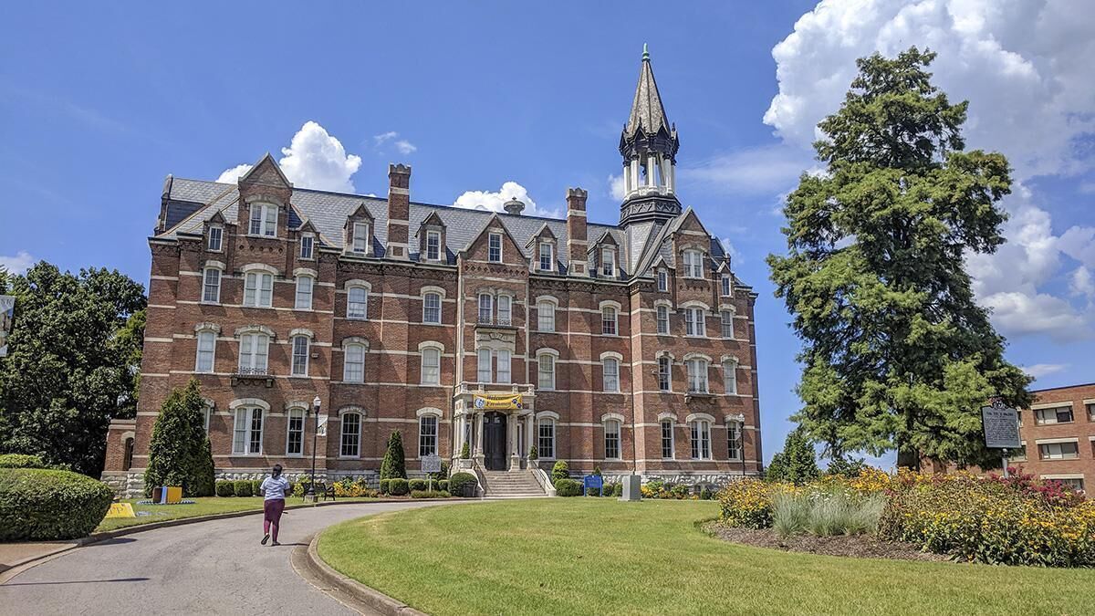Een groot bakstenen gebouw met een opvallende toren en een verzorgd gazon.