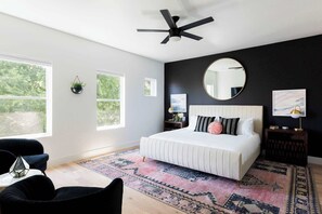 Un dormitorio con una cama grande, un ventilador de techo, un espejo redondo y vistas a zonas verdes.