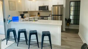 Una cucina moderna con mobili bianchi, elettrodomestici in acciaio inossidabile e un'isola centrale con sgabelli da bar.