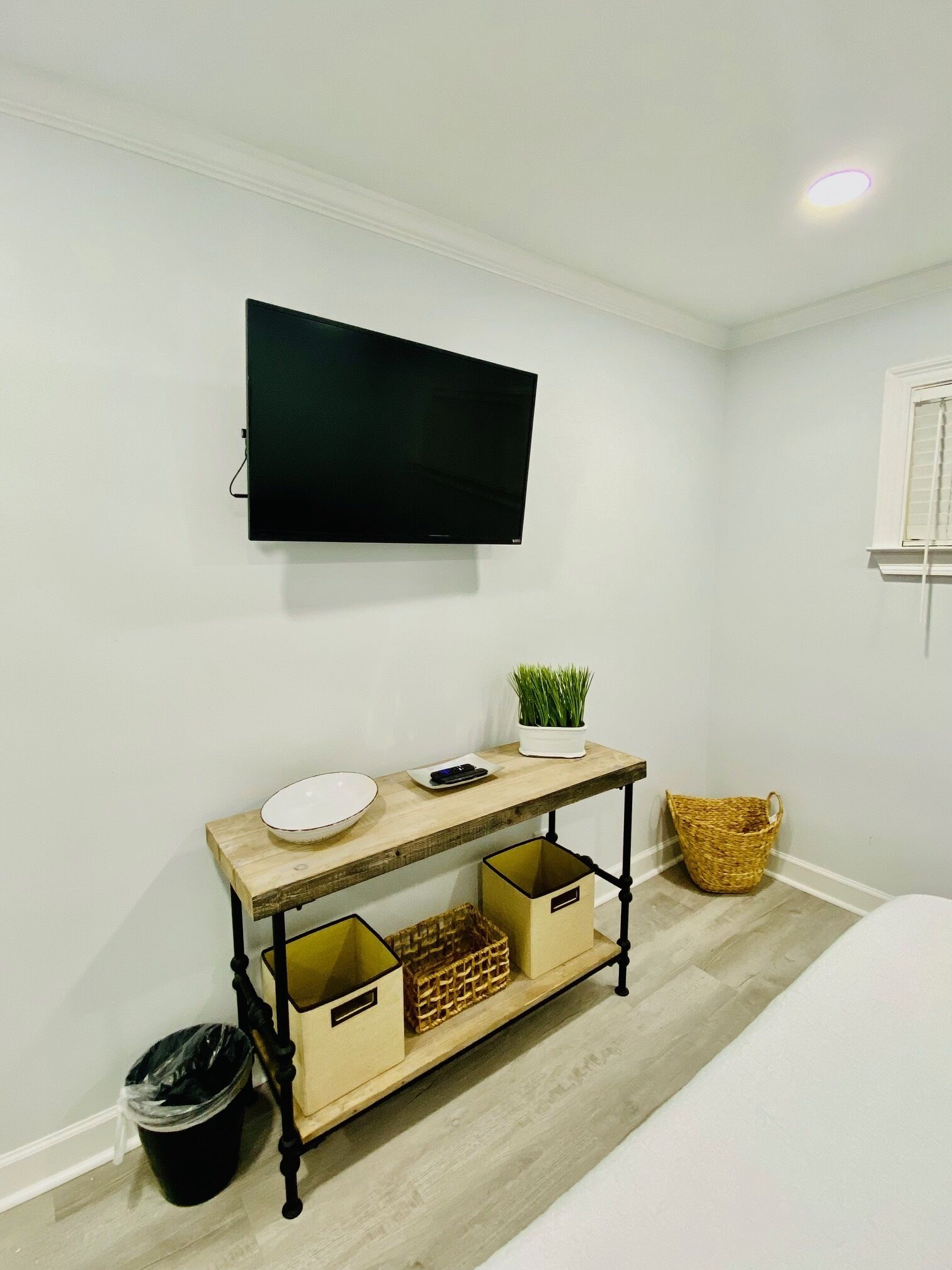 A room with a mounted TV, a wooden console table with storage, a small plant, and a wicker basket.