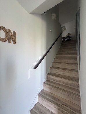 A staircase with wooden steps and a handrail, a wall with a wooden 'N' decoration, and a small table with a sign in the background.