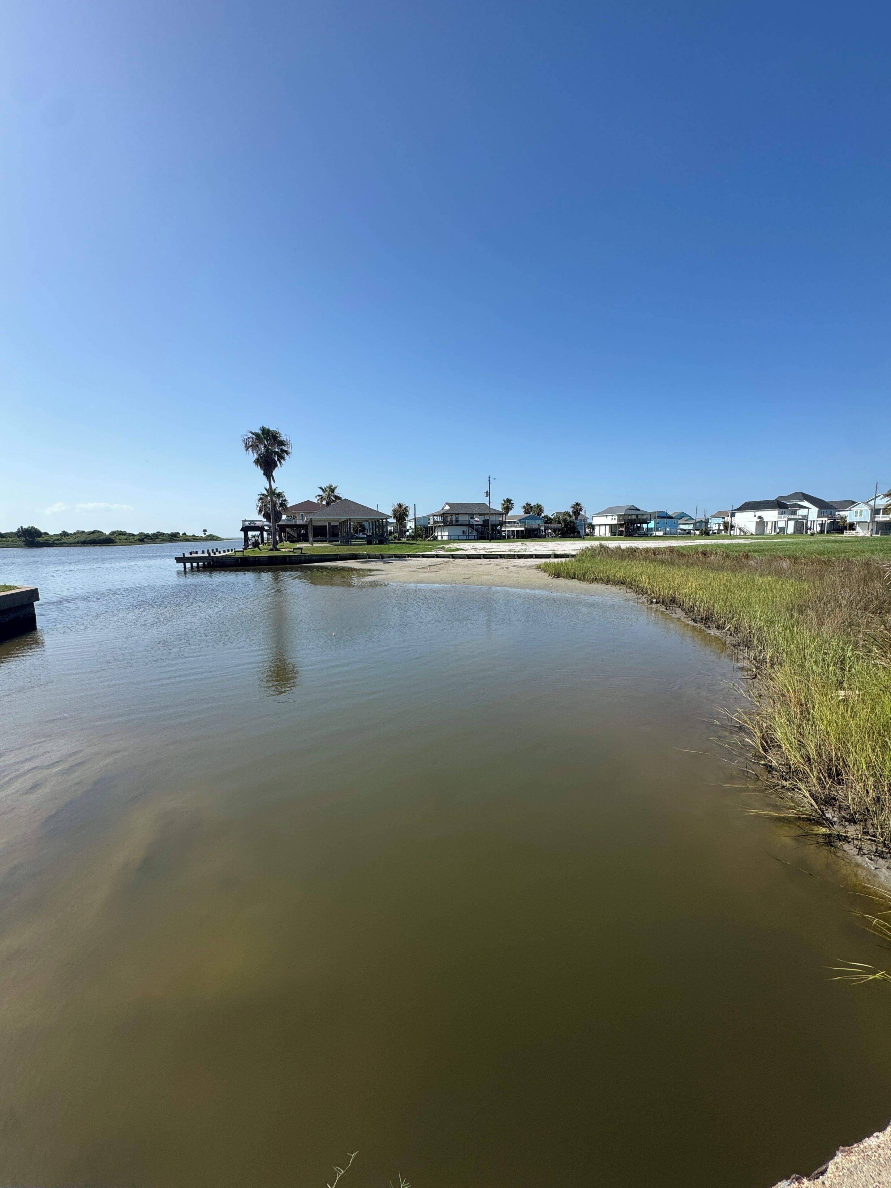 A calm water body with a dock, a small pavilion, and houses in the background.