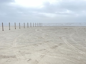Una playa arenosa con huellas e impresión de neumáticos, estacas de madera y un cielo nublado.