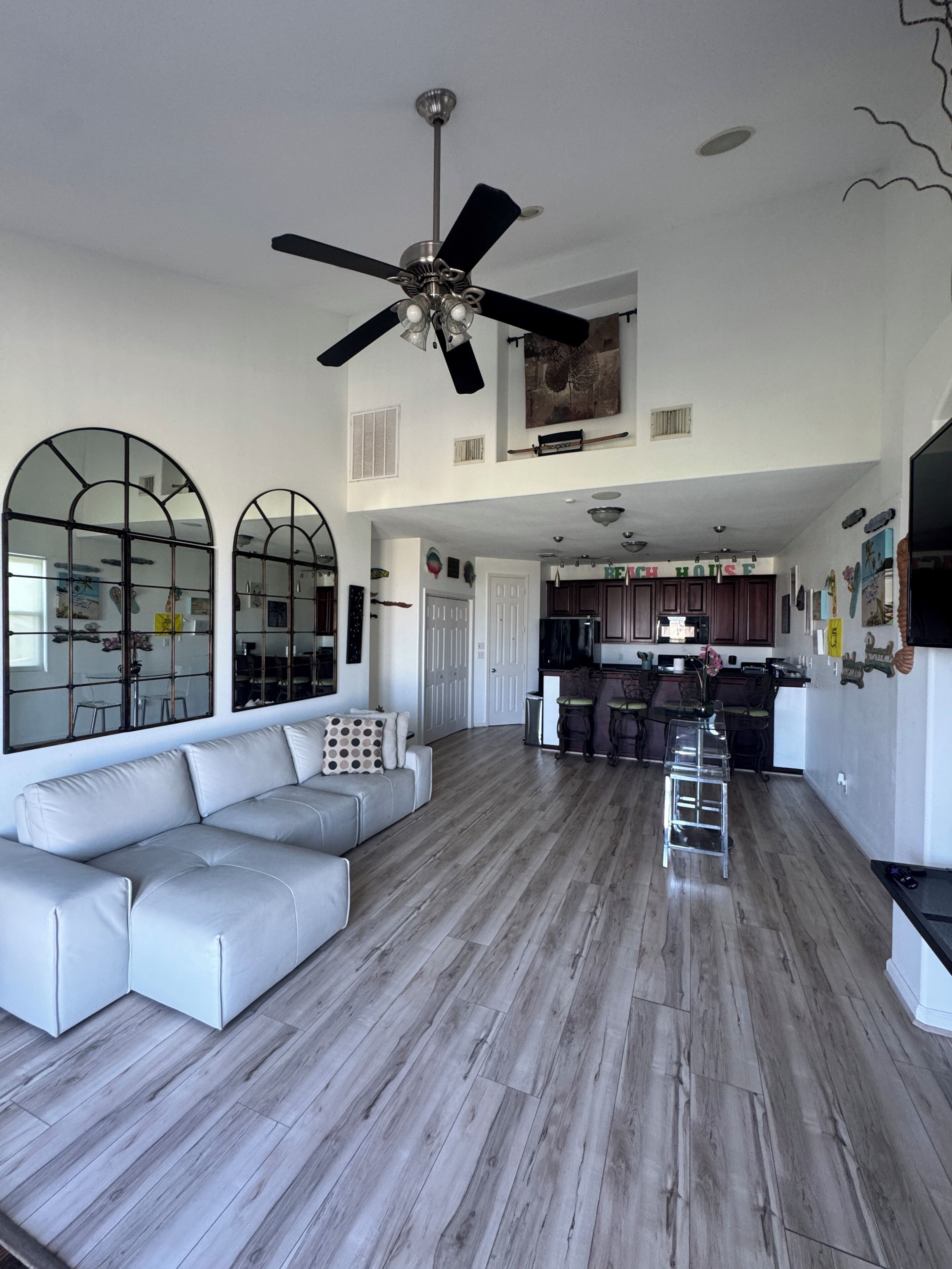 A spacious living area with a ceiling fan, a sofa, and a kitchen in the background.