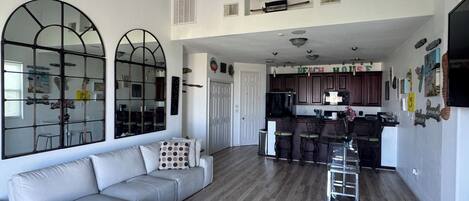 A spacious living area with a ceiling fan, a sofa, and a kitchen in the background.
