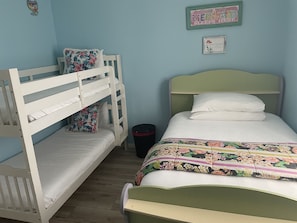 Habitación con literas, un cojín floral, un cuadro enmarco y un cesto de basura.