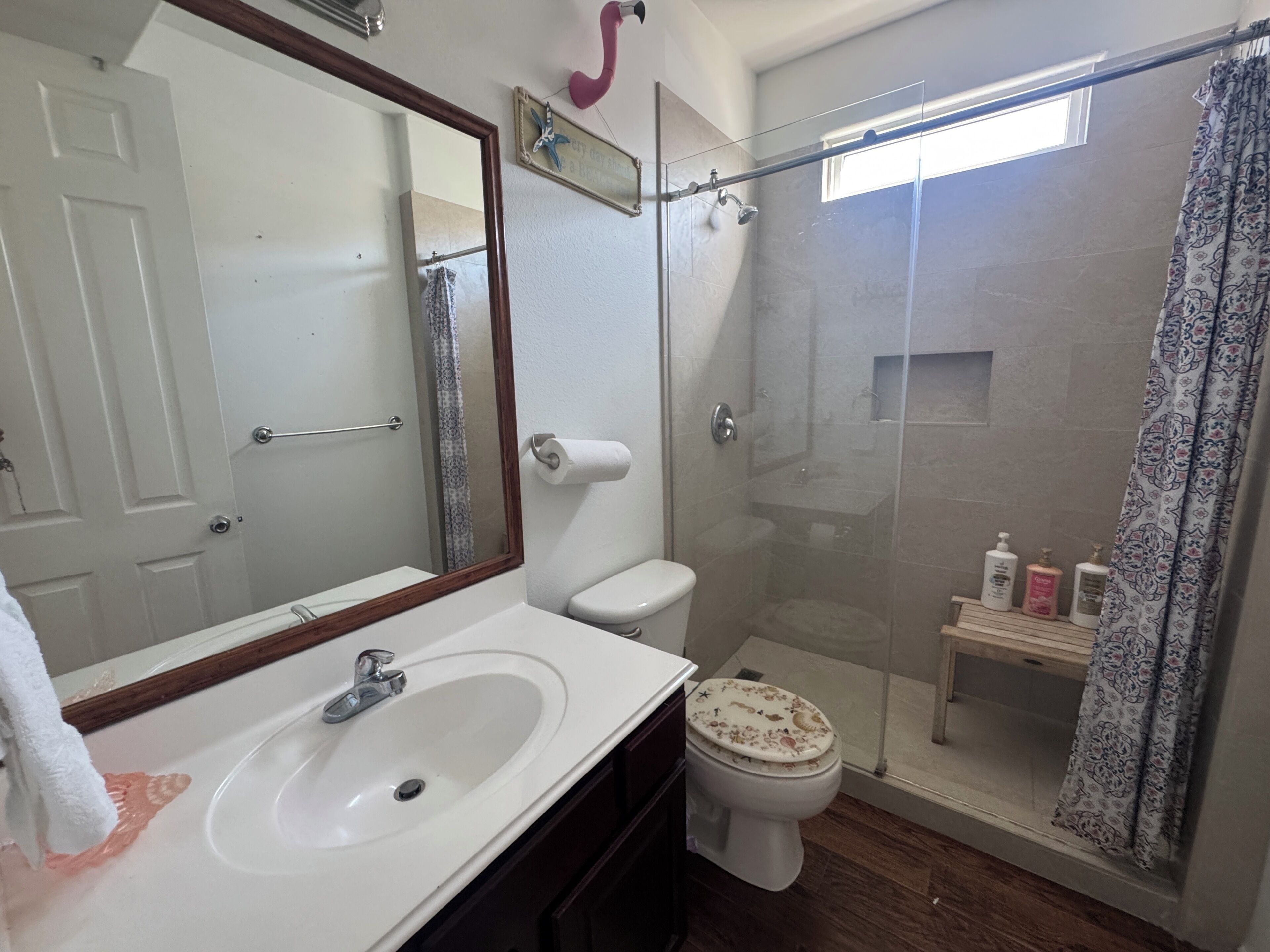 A bathroom with a white sink, a toilet, a glass-enclosed shower, and a mirror with a wooden frame.
