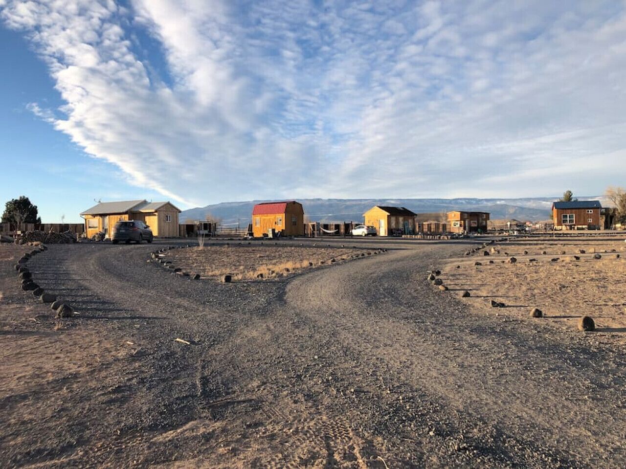 A rural road with houses on either side, a clear sky, and distant mountains.