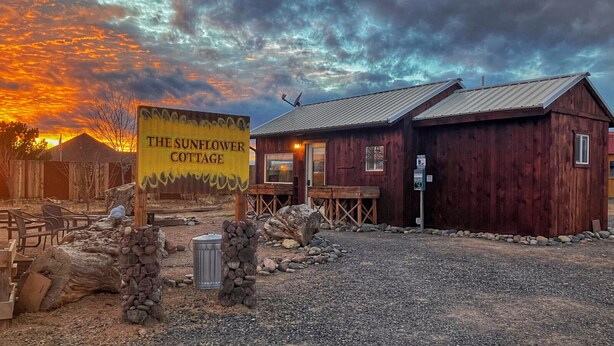 Een rustiek houten gebouw, genaamd 'The Sunflower Cottage', met een grindpad en een houten bankje.