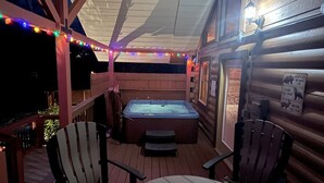 Un interior cálido de cabaña con jacuzzi, terraza de madera y luces colgantes.