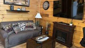 Una sala de estar acogedora con un sofá marrón, una mesa de centro de madera, una chimenea, un televisor y un reloj en la pared.