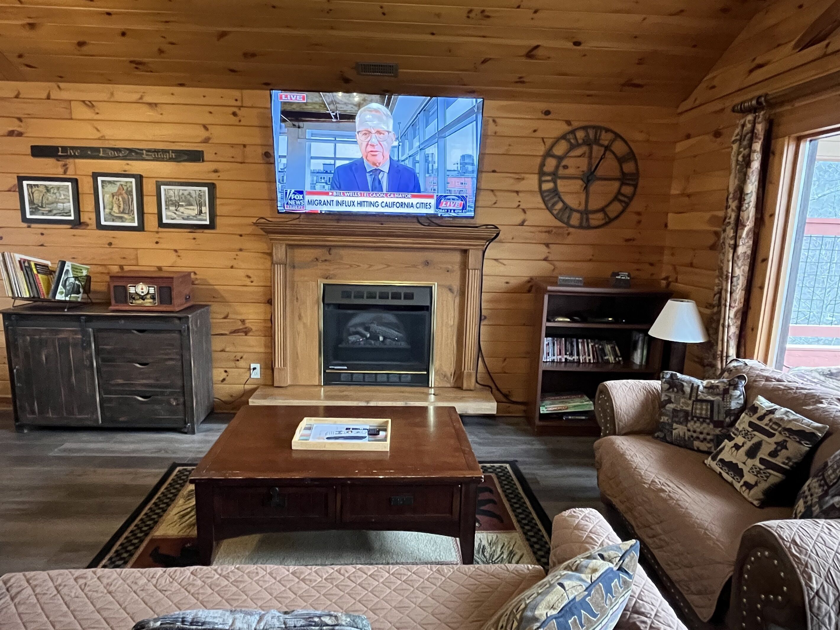 A cozy living room with a fireplace, a television mounted above it, and a clock on the wall.