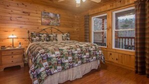 Une chambre dans une cabane en bois, avec un lit, une table de chevet, un ventilateur de plafond et une fenêtre avec des rideaux.