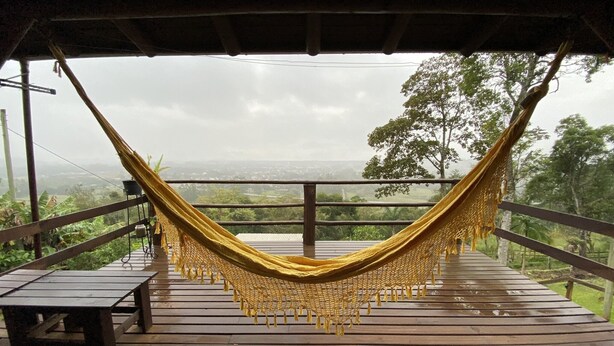 Un hamac sur une terrasse en bois, avec vue sur un paysage verdoyant.