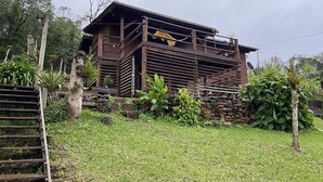 Une maison en bois dotée d’un balcon, entourée d’une végétation luxuriante et d’un mur de pierre.