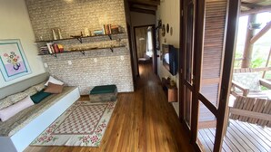 Un salon chaleureux avec un plancher en bois, un canapé agrémenté de coussins, un tapis à motifs et un mur en briques orné d’étagères où sont disposés des livres et des objets décoratifs.