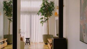 A room with two large potted bamboo plants, a black stool, a small wooden table, and a large painting on the wall. - Monument House (Daylesford)