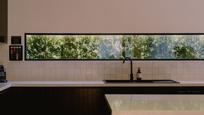 A modern kitchen with a large window, a black faucet, and a coffee machine. - Monument House (Daylesford)