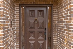 A brown door with decorative panels and a brass knocker, set in a brick wall.