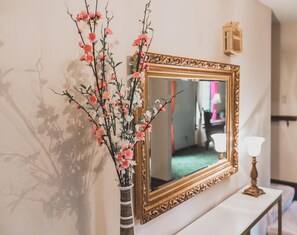 A mirror with an ornate gold frame, a vase with pink flowers, and a small table with a lamp.