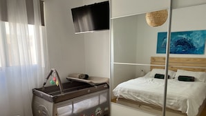 Hotellihuone, jossa on sänky, pieni työpöytä, peili ja seinälle asennettu televisio.