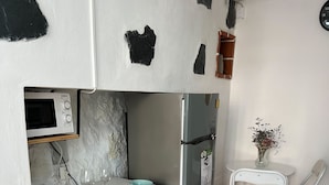 Kompakti keittiö, jossa on mikroaaltouuni, jääkaappi ja pieni ruokailutila, jossa on baarituoleja.
