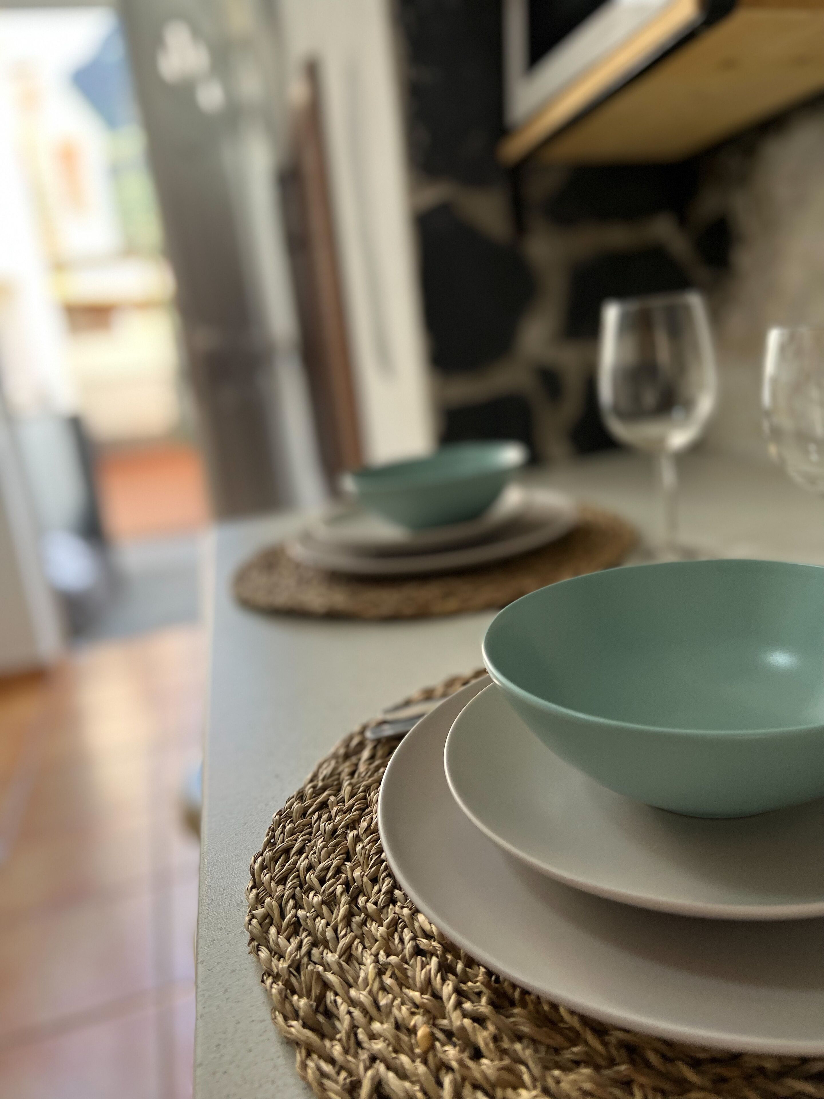 Una mesa de comedor con un mantel tejido, un bol color turquesa y una copa de vino.