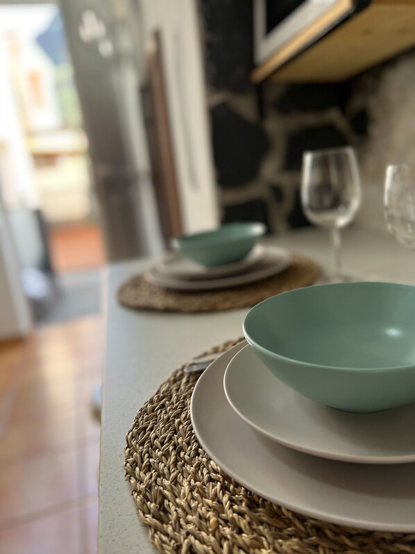 A dining table with a woven placemat, a teal bowl, and a wine glass.