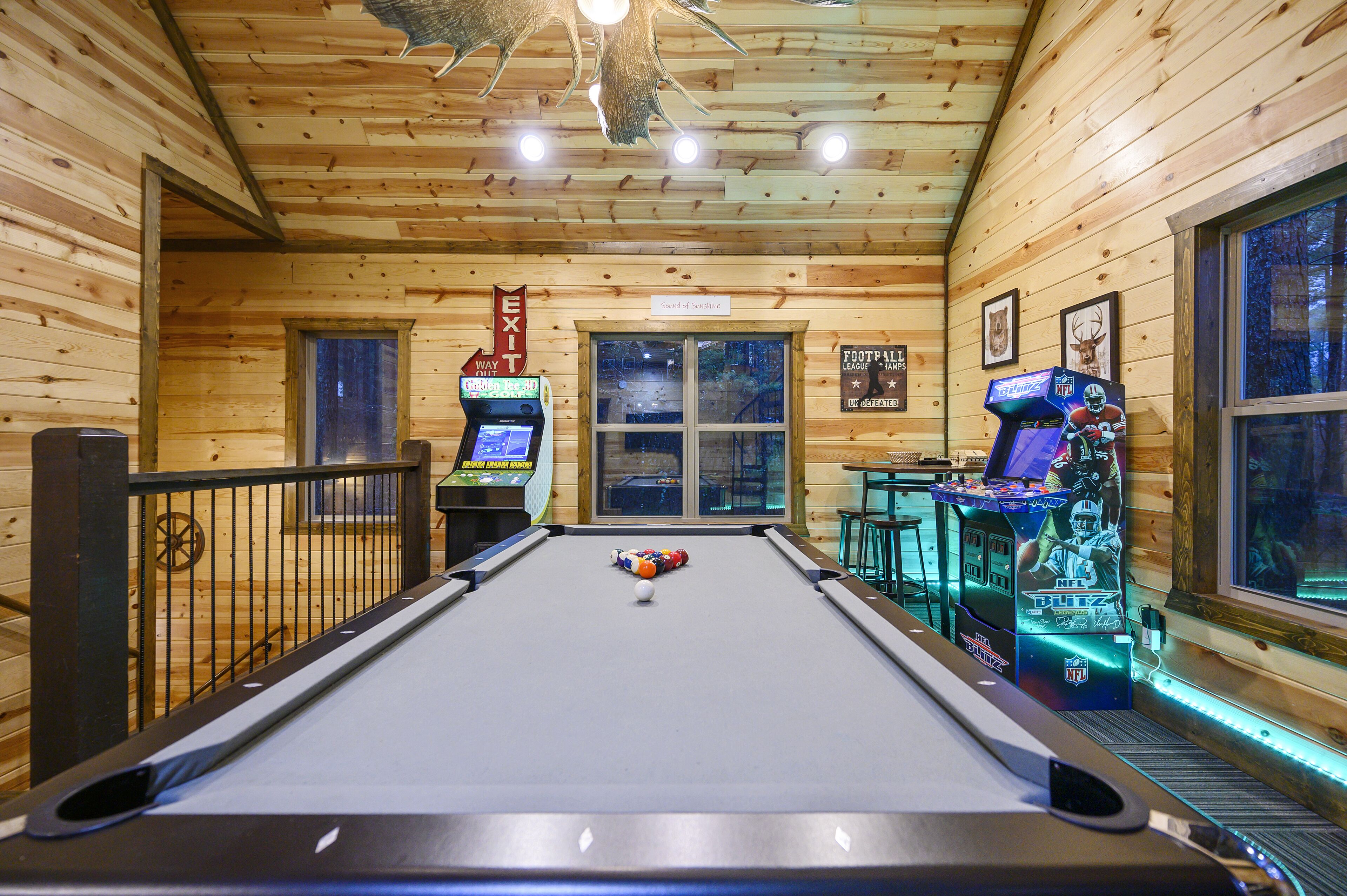 A pool table with billiard balls, a pool table, and two video game machines.