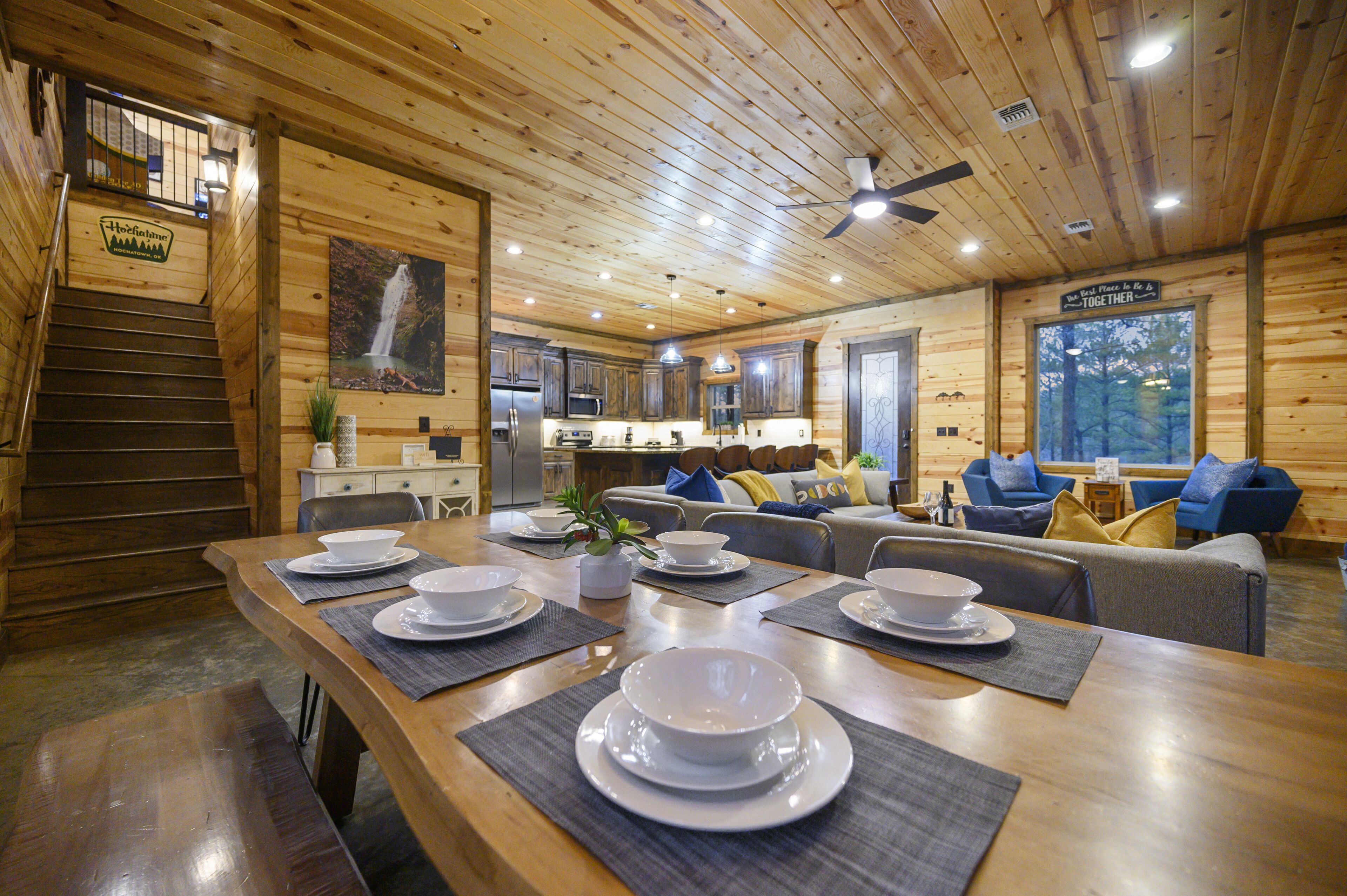 L’intérieur d’un chalet en bois comprend un coin repas aménagé pour quatre personnes, une cuisine et un salon avec un canapé et des fauteuils bleus.