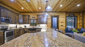Un'ampia cucina con ripiani in granito, mobili in legno e un'isola grande. Sono presenti elettrodomestici integrati, tra cui un forno a microonde e un forno, e una zona pranzo con un divano e sedie.