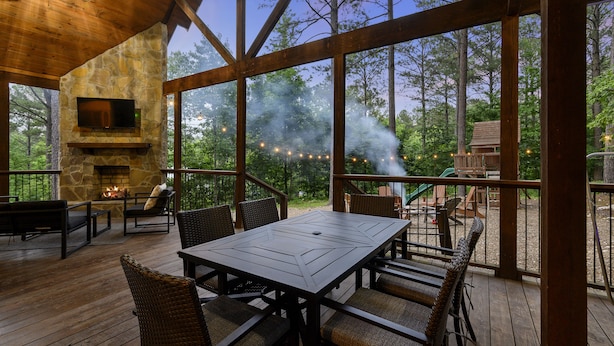Una terrazza esterna con un camino in pietra, mobili in legno e vista sulla foresta.