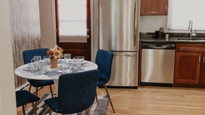 Une cuisine moderne dotée d’un réfrigérateur en acier inoxydable, de meubles en bois et d’un coin repas avec des chaises bleues et une table dressée pour quatre personnes.
