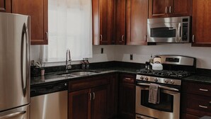 Une cuisine avec des meubles en bois, des appareils électroménagers en acier inoxydable, une fenêtre avec un rideau et un évier.