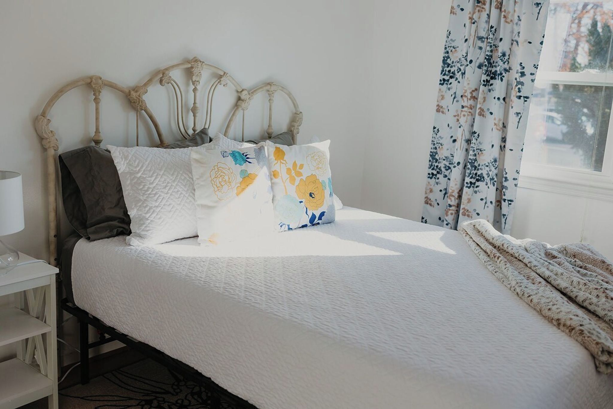 A bed with a white quilt, a dark throw, and floral-patterned pillows.