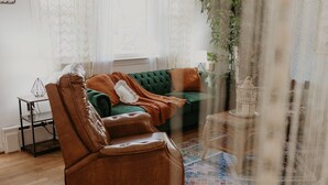 Un salon chaleureux avec un fauteuil en cuir, un canapé vert et un tapis à motifs.