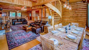 A log cabin interior with a dining area, leather seating, and a spiral staircase.