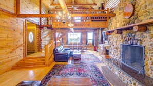 A log cabin interior with a stone fireplace, wooden staircase, and a cozy seating area.