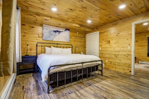 A wooden-paneled bedroom with a metal bed frame, a white bedspread, and a painting on the wall. - Breathtaking Cabin & Views (Conway)