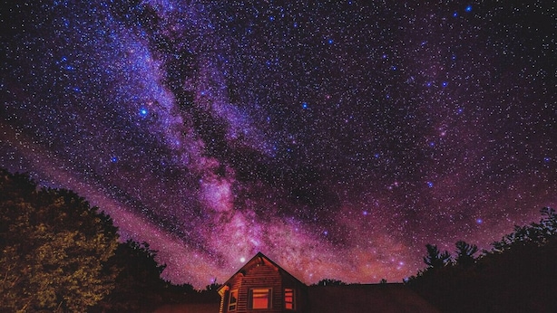 A rustic cabin with a porch under a starry night sky.