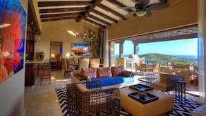 A spacious living room with a large window overlooking a scenic view, furnished with sofas and chairs, and a ceiling fan. - Beautiful Golf Villa 2 Puerto Los Cabos (Puerto Los Cabos)