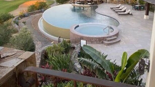 A pool area with a hot tub, lounge chairs, and a thatched-roof structure, surrounded by tropical plants and a scenic view of mountains and golf course. - Beautiful Golf Villa 2 Puerto Los Cabos (Puerto Los Cabos)