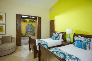 A hotel room with two beds, a sitting area, and a view of a courtyard with a fountain.