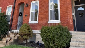 A red brick building with white-framed windows, a black door with a 'welcome' sign, and a small staircase leading to the entrance. - Soulard|Completely new home|Walkability (St. Louis)