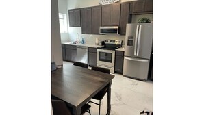 A modern kitchen with dark cabinets, stainless steel appliances, and a marble floor. - Soulard|Completely new home|Walkability (St. Louis)