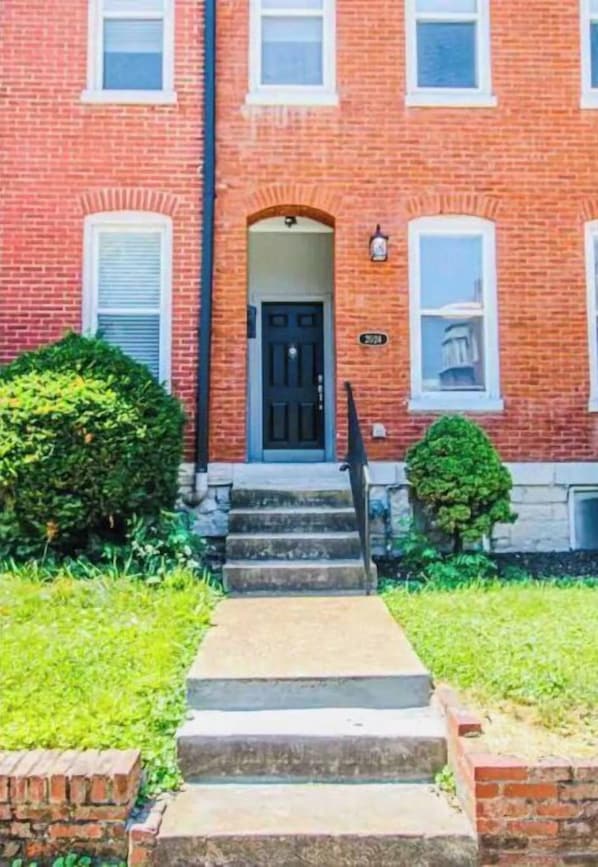 A red brick building with a black front door, a small porch, and steps leading to the entrance.