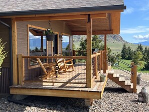 A wooden cabin with a porch, outdoor seating, and a staircase leading to a deck. - Little Juniper Cabin (Ennis)