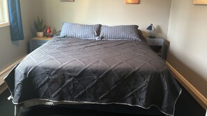Una cama bien hecha con una cubierta acolchada, una lámpara de noche y una mesita de noche con una planta.