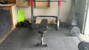 Un gimnasio en casa con una prensa de banca, barra y discos de pesas.